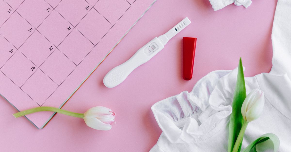 Flat lay of a pregnancy test with tulips on a pink calendar surface, symbolizing fertility and new life.